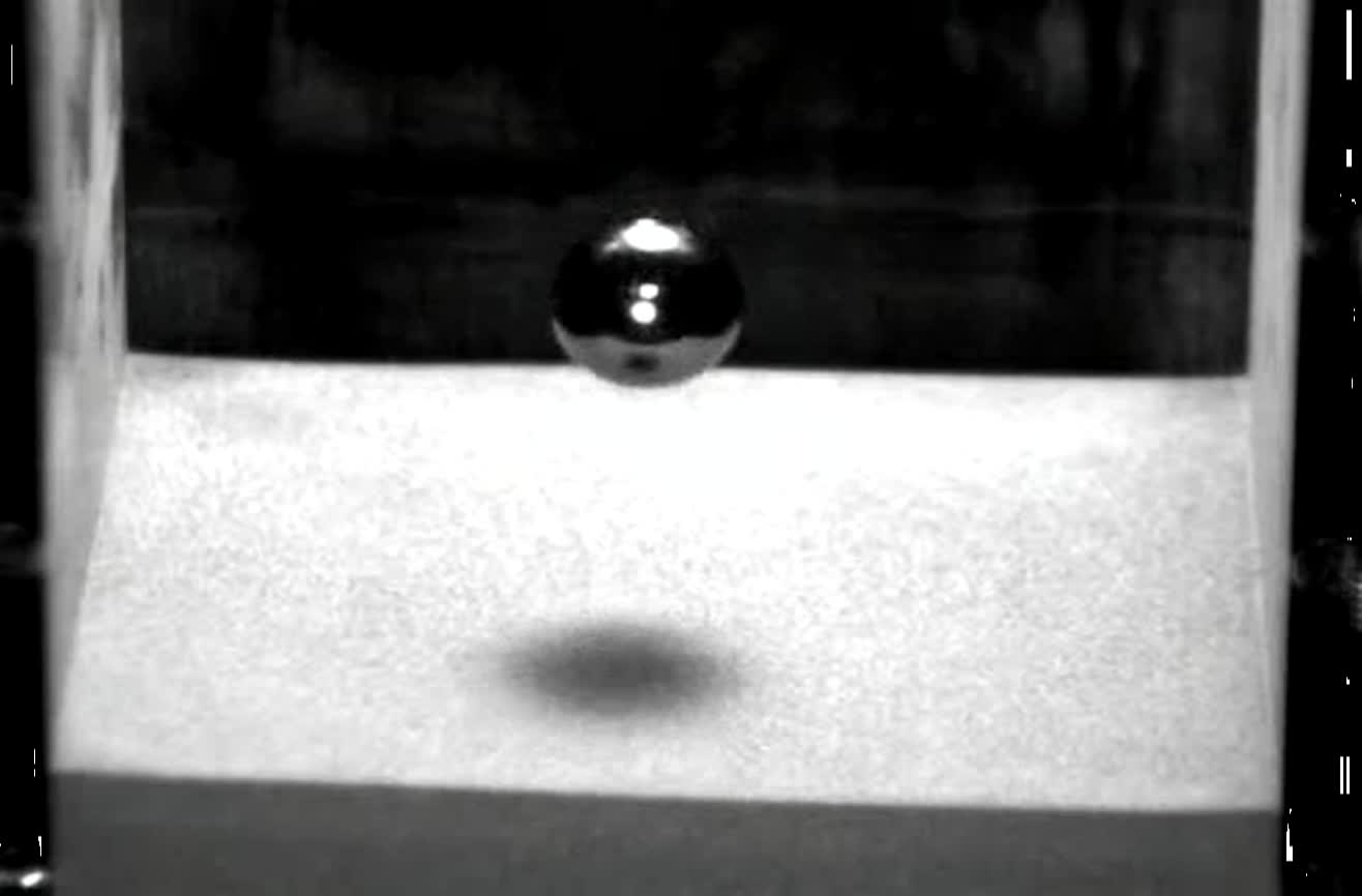 A metal ball hitting sand in slow motion.